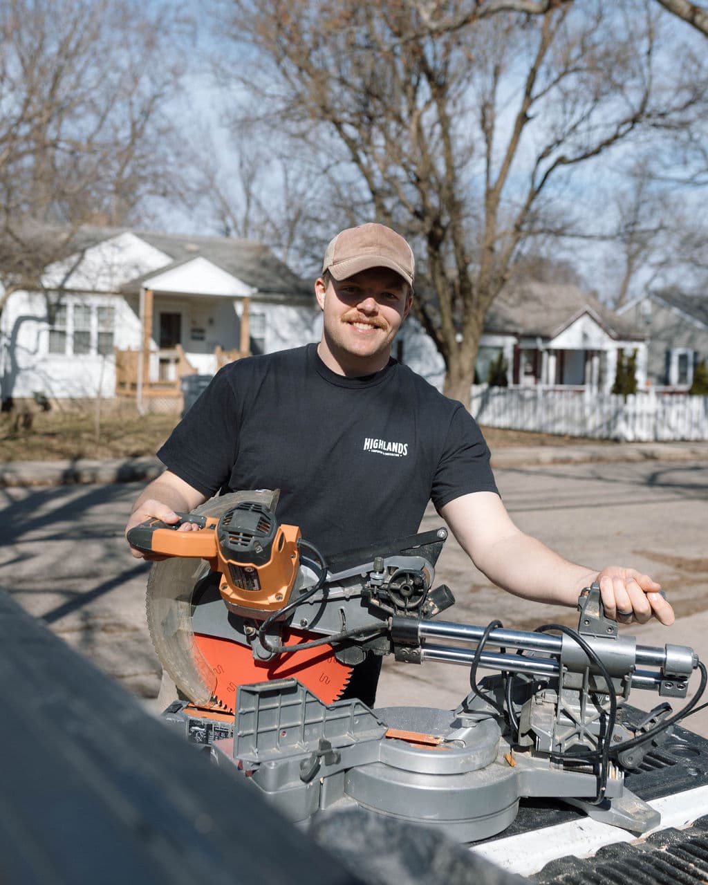 Adam Ginn holding a miter saw beside his work truck